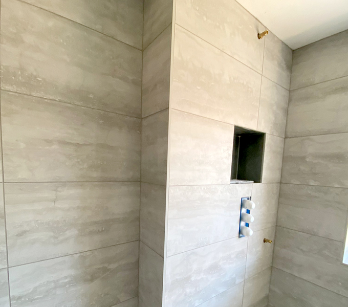 large rectangular textured beige tiles in a bathroom with a cubby hole on the shower wall