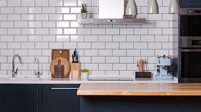 a kitchen with white tiles on the walls with a polished wooden countertop and navy doors
