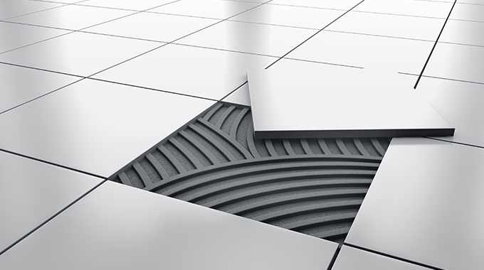 a white tiled floor with one tile diagonally over a gap with thinset mortar spread in the gap